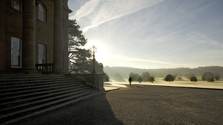 Berrington Hall, Herefordshire, is in shadow in the foreground, while a visitor walks along the drive away from the house.